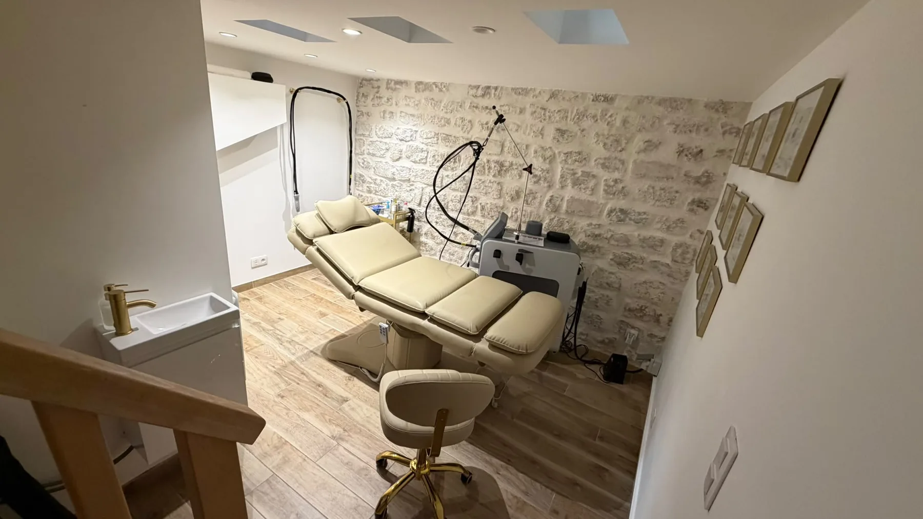 La salle de soins : fauteuil de soin crème, laser Candela, mur de pierre blanchi et robinetterie laiton